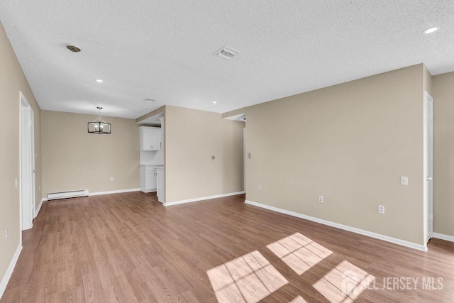 spare room featuring light wood-type flooring, a baseboard radiator, baseboards, and a textured ceiling