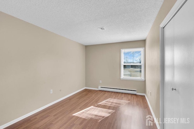 unfurnished bedroom featuring a baseboard heating unit, a closet, baseboards, and wood finished floors