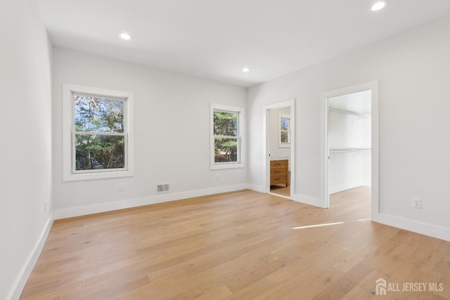 unfurnished bedroom featuring a spacious closet, connected bathroom, and light wood-type flooring