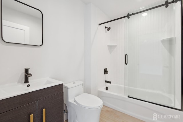 full bathroom with hardwood / wood-style flooring, bath / shower combo with glass door, vanity, and toilet