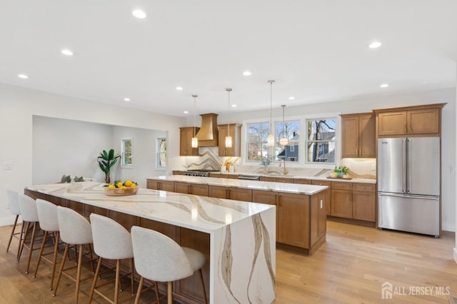 kitchen with premium range hood, light wood-type flooring, appliances with stainless steel finishes, pendant lighting, and a large island