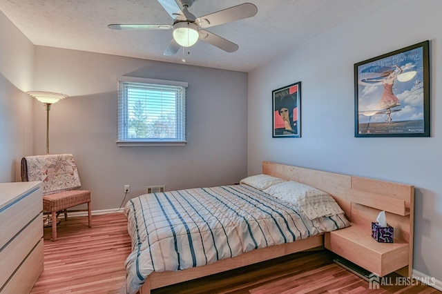 bedroom with ceiling fan, a textured ceiling, visible vents, baseboards, and light wood-style floors