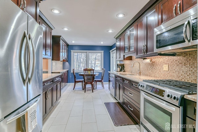 kitchen featuring appliances with stainless steel finishes, a sink, light stone counters, and dark brown cabinetry