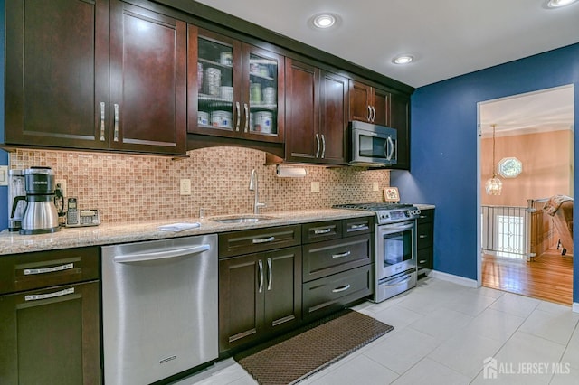 kitchen featuring light stone counters, decorative backsplash, appliances with stainless steel finishes, dark brown cabinetry, and a sink