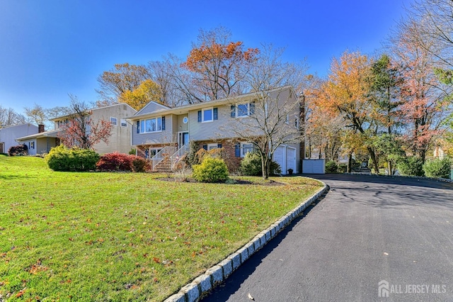 split foyer home with driveway, a garage, a front lawn, and brick siding