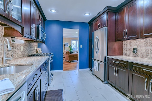 kitchen featuring light stone counters, dark brown cabinetry, a sink, baseboards, and appliances with stainless steel finishes