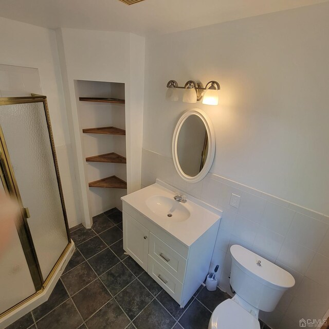 bathroom with walk in shower, toilet, tile walls, vanity, and tile patterned flooring