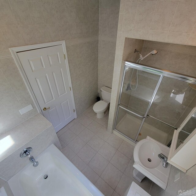 bathroom with toilet, a shower with shower door, tile patterned flooring, and tile walls