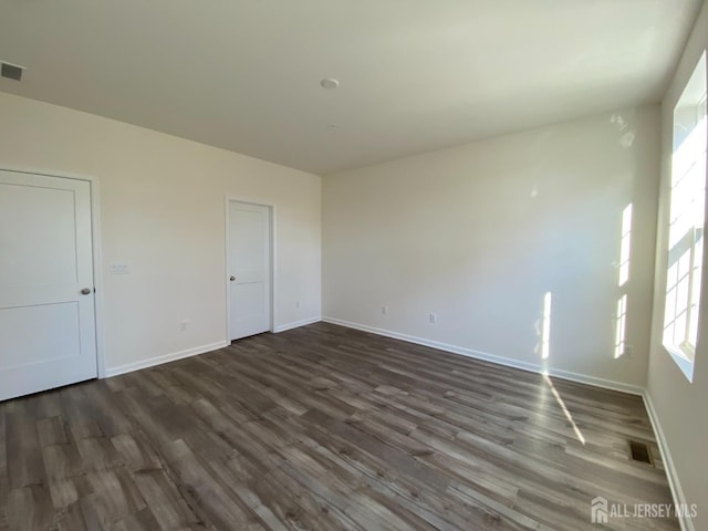 spare room with dark wood-style floors, visible vents, and baseboards