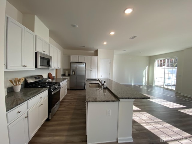 kitchen with sink, dark stone countertops, a kitchen island with sink, white cabinets, and appliances with stainless steel finishes