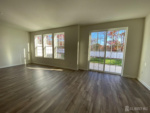 unfurnished living room featuring baseboards, a healthy amount of sunlight, and dark wood-style flooring