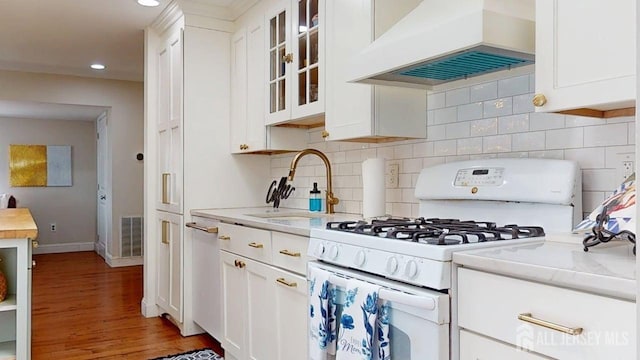 496 Calvert Rd, North Brunswick, NJ 08902 - kitchen with white gas stove, custom exhaust hood, a sink, white cabinets, and light wood-style floors