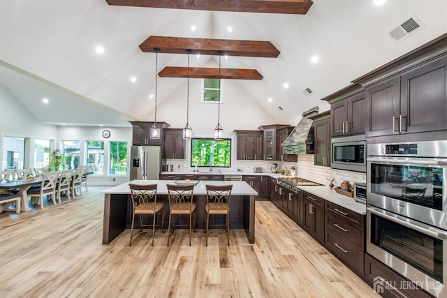 kitchen with appliances with stainless steel finishes, backsplash, wall chimney range hood, high vaulted ceiling, and a kitchen island