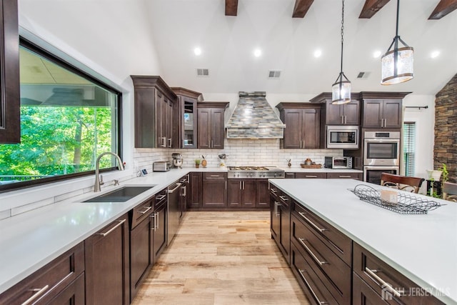 kitchen with decorative backsplash, wall chimney exhaust hood, stainless steel appliances, sink, and decorative light fixtures