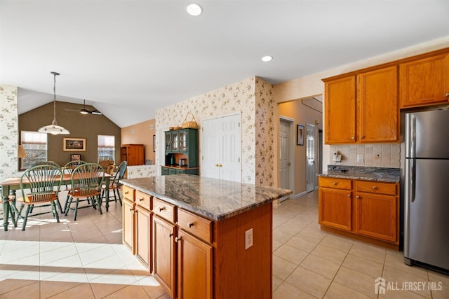 kitchen featuring pendant lighting, dark stone counters, stainless steel fridge, and a center island