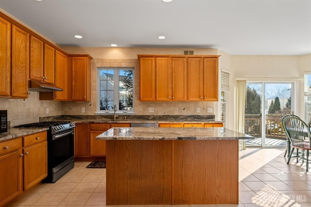 kitchen featuring a kitchen island, stone countertops, backsplash, light tile patterned floors, and stainless steel gas range