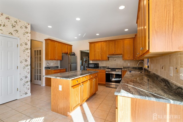 kitchen with sink, stainless steel appliances, dark stone counters, and a kitchen island