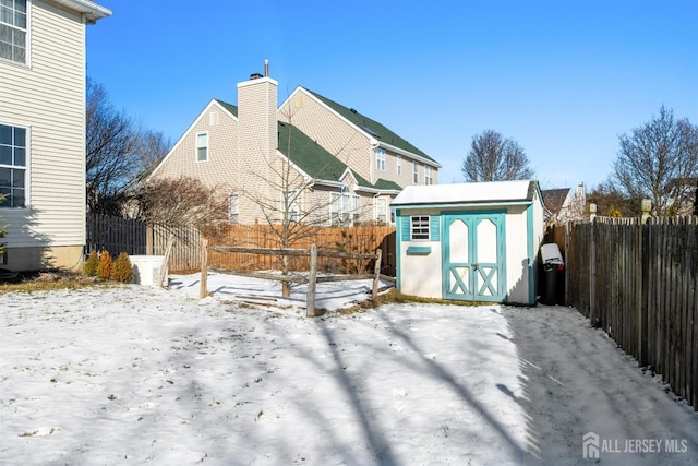 snow covered back of property featuring a storage shed