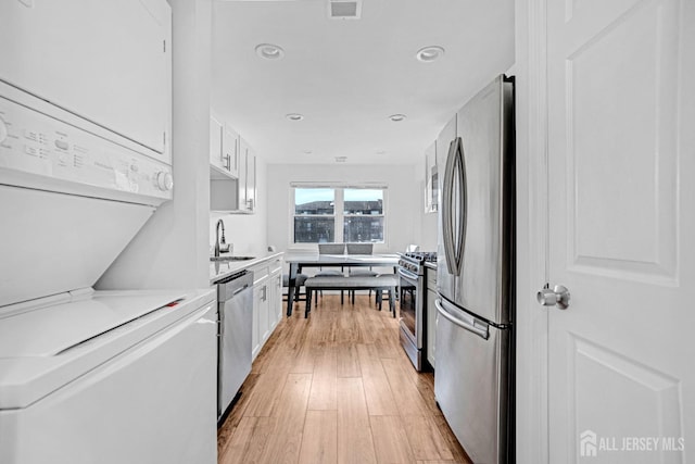 529 Sharon Garden Ct, Woodbridge Proper, NJ 07095 - kitchen featuring stacked washing machine and dryer, appliances with stainless steel finishes, white cabinetry, light countertops, and light wood-style floors