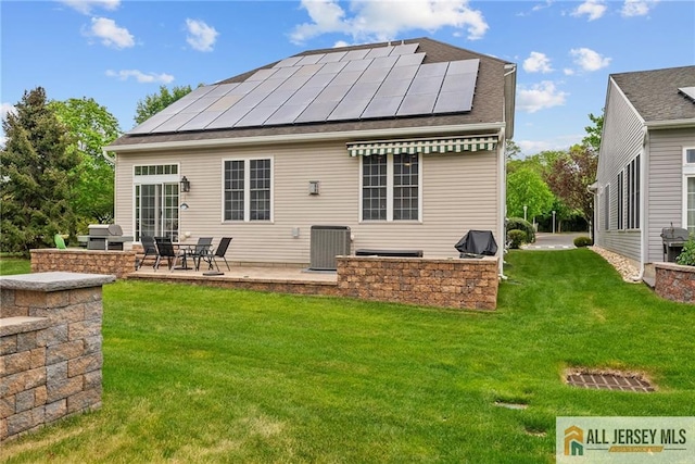 rear view of house with solar panels, a lawn, a patio, and central AC
