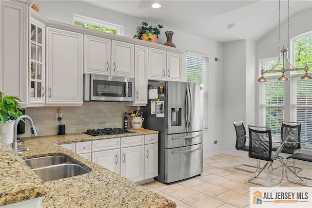 kitchen with appliances with stainless steel finishes, a sink, tasteful backsplash, glass insert cabinets, and light stone counters