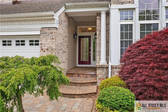 view of exterior entry featuring a shingled roof and a garage