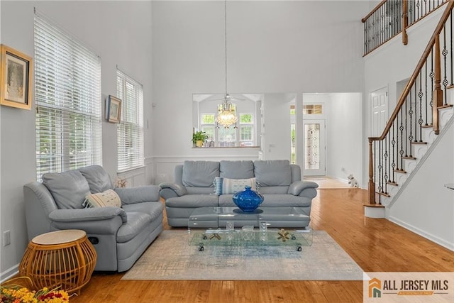 living room with a towering ceiling, stairway, a chandelier, and wood finished floors