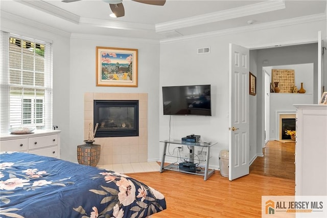bedroom featuring a fireplace, a tray ceiling, light wood finished floors, crown molding, and baseboards
