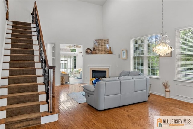living room with a towering ceiling, stairs, wood finished floors, a chandelier, and a lit fireplace