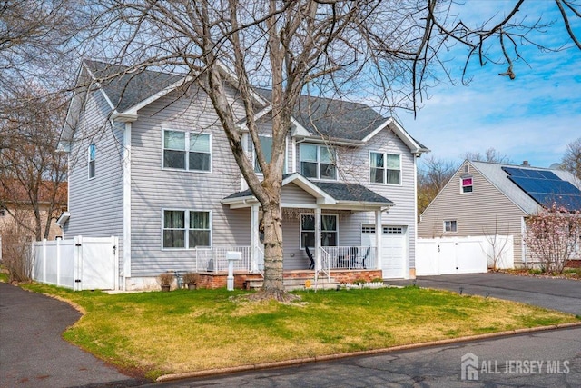 traditional-style home with a garage, aphalt driveway, fence, covered porch, and a front yard