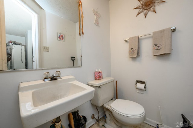 half bath with a textured ceiling, toilet, baseboards, and a sink