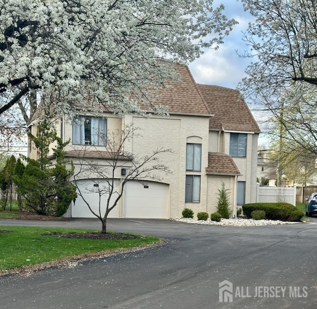 view of front of home featuring stucco siding, driveway, a shingled roof, fence, and an attached garage