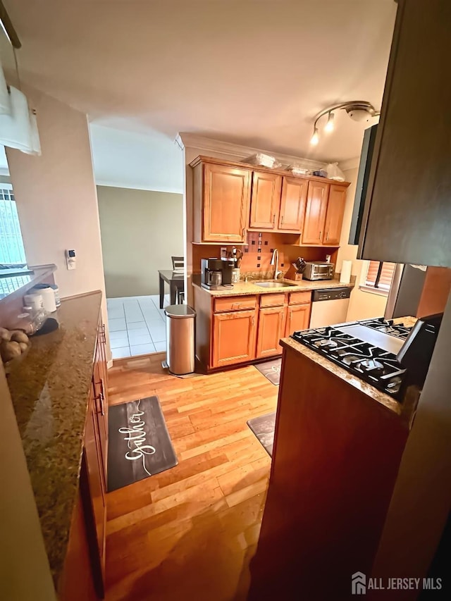 kitchen with a sink, light wood-style flooring, dishwasher, light brown cabinetry, and light stone counters