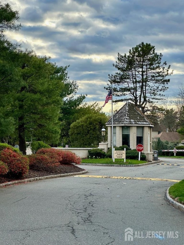 view of asphalt road featuring curbs, traffic signs, and a gated entry