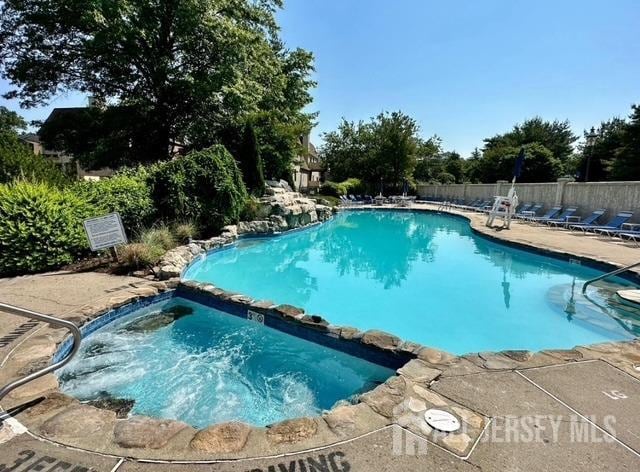 view of swimming pool featuring a pool with connected hot tub and fence
