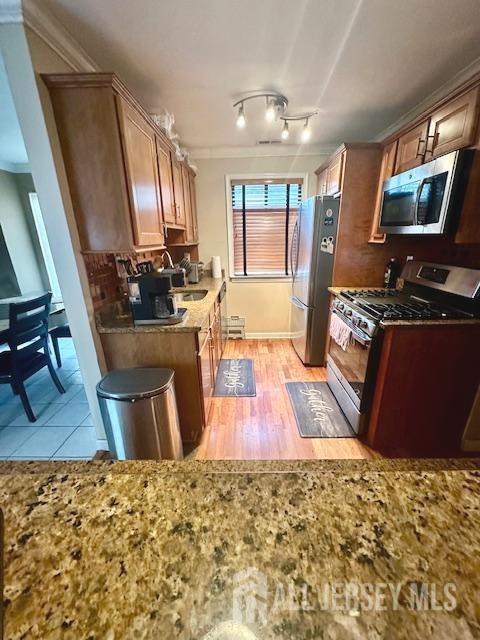 kitchen featuring stainless steel appliances, a sink, light stone counters, crown molding, and light wood-type flooring