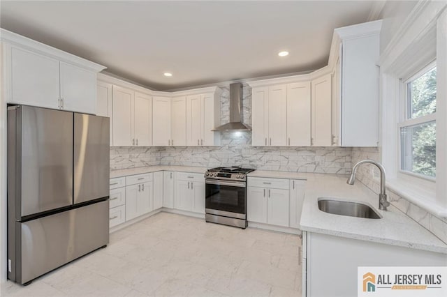 kitchen featuring light stone counters, stainless steel appliances, wall chimney range hood, white cabinets, and sink