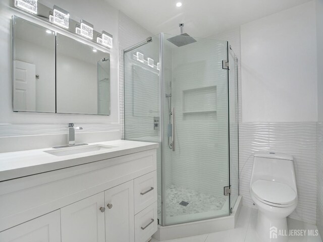 bathroom with vanity, a shower with shower door, tile walls, and toilet