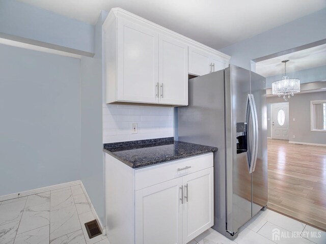 kitchen featuring dark stone countertops, stainless steel fridge, white cabinets, backsplash, and hanging light fixtures