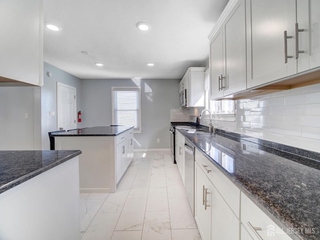 kitchen featuring white cabinetry, appliances with stainless steel finishes, a kitchen island, and dark stone countertops