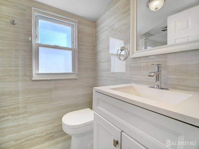 bathroom featuring vanity, toilet, tile walls, and a shower