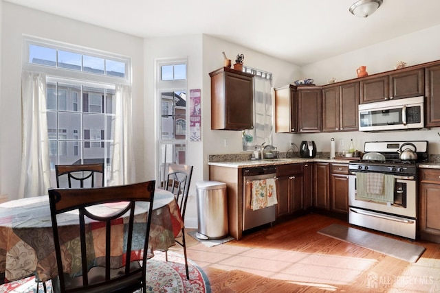 kitchen featuring sink, light hardwood / wood-style flooring, light stone counters, dark brown cabinetry, and stainless steel appliances