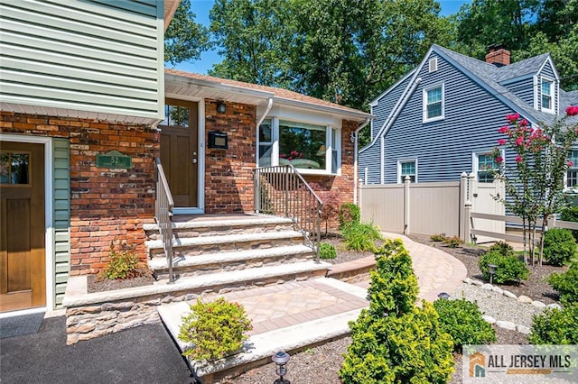 view of exterior entry featuring fence, a chimney, brick siding, and roof with shingles