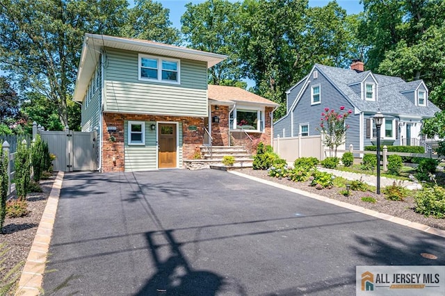 view of front of property featuring a gate, fence, brick siding, and asphalt driveway