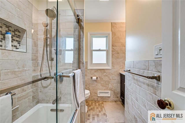 bathroom with tile walls, bath / shower combo with glass door, and toilet
