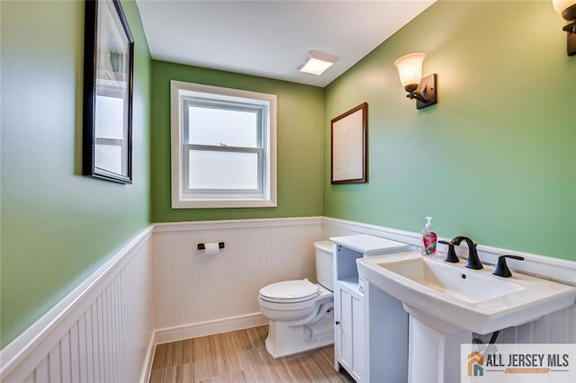 half bathroom featuring a wainscoted wall, toilet, and wood finished floors