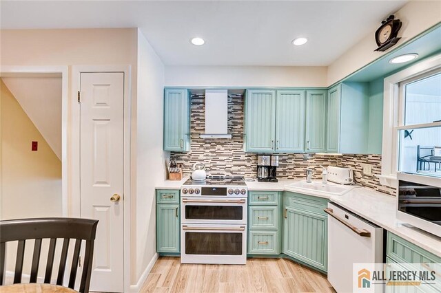 kitchen featuring double oven range, white dishwasher, a sink, light countertops, and light wood-style flooring