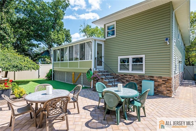 rear view of house featuring outdoor dining area, a patio area, a sunroom, entry steps, and stone siding
