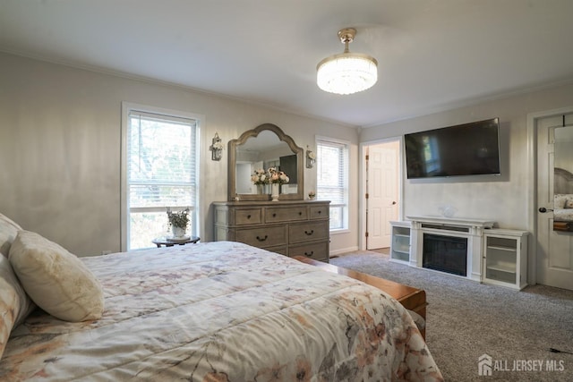 carpeted bedroom featuring a glass covered fireplace and crown molding