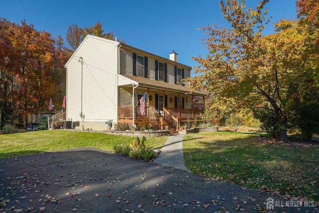 traditional-style house with stairs, a front yard, a chimney, and covered porch